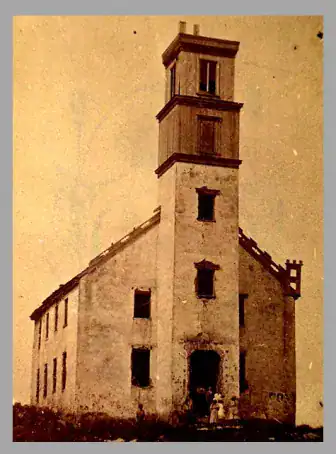 An old, weathered church with a tall belfry tower, partially deteriorating, stands isolated. Two people are visible near the entrance.
